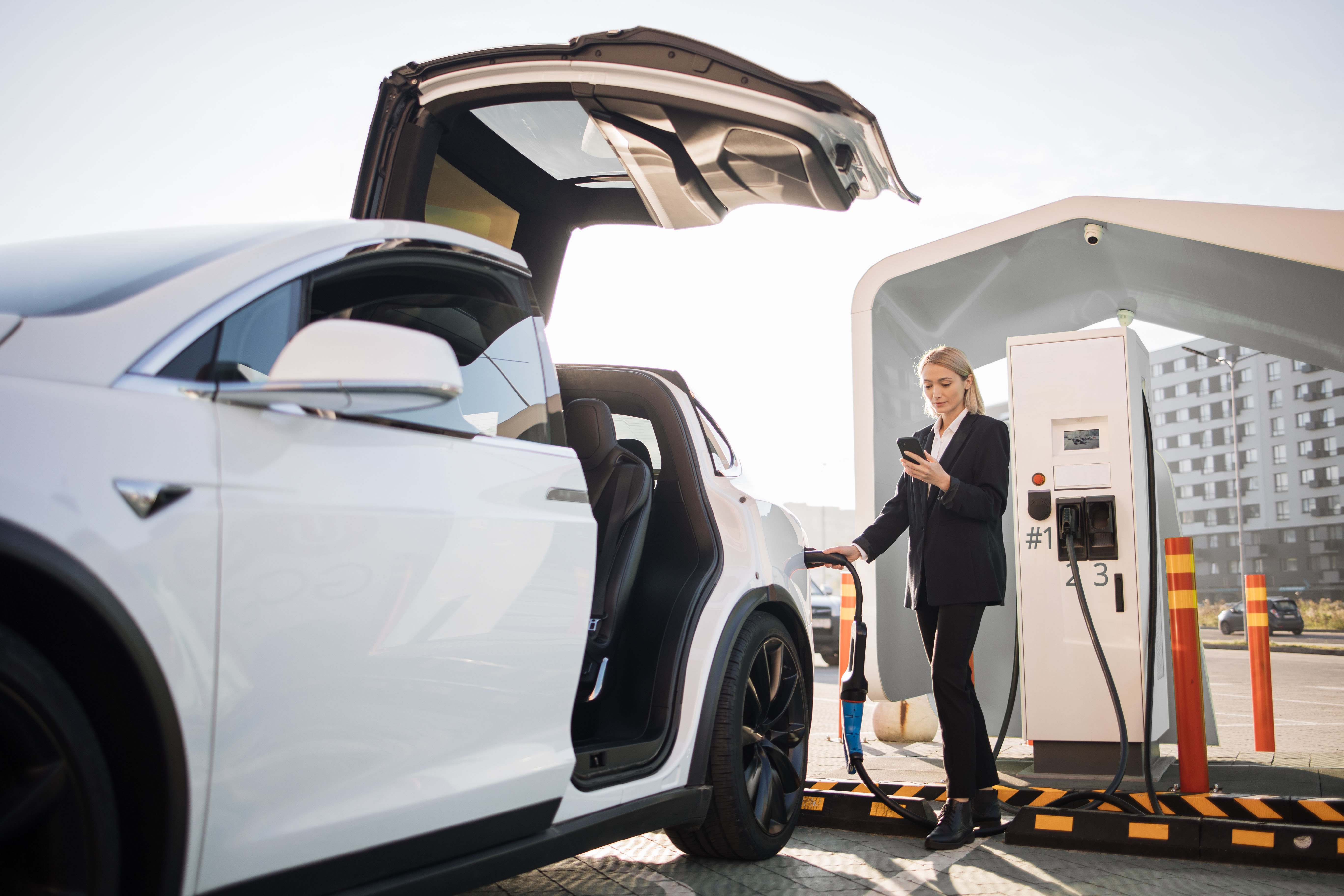 woman-using-smartphone-and-charging-car-outdoors-2024-12-13-13-58-10-utc